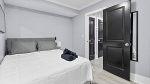 A bedroom with a bed, grey pillows, a white bedspread, and a rolled towel on the bed. There are two doors, one open and one closed, leading to another room. - New DC Unit+Prime Location+2BR+Private Parking (Washington)