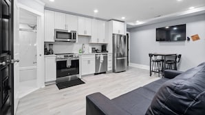 A modern kitchen with white cabinets, stainless steel appliances, and a dining area with a black table and chairs. - New DC Unit+Prime Location+2BR+Private Parking (Washington)