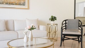 A living room with a round glass coffee table, a white sofa, a black and white checkered chair, and a small side table with a plant. - WaterView 4 miles to Disney 3Br 2Ba Pool Home (Kissimmee)