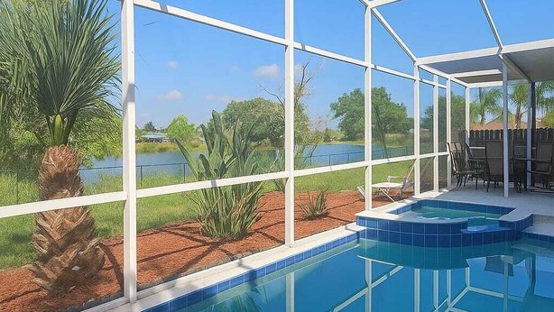 A swimming pool with a glass enclosure, surrounded by palm trees and a view of a lake. - WaterView 4 miles to Disney 3Br 2Ba Pool Home (Kissimmee)