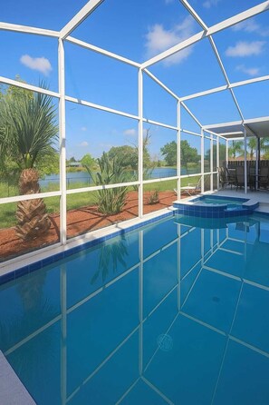 A swimming pool with a glass enclosure, surrounded by palm trees and a view of a lake.