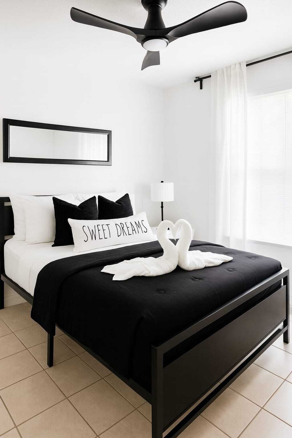 A modern bedroom with a black bed, white pillows, a sign reading 'SWEET DREAMS,' a white swan decoration, a ceiling fan, and a nightstand with a lamp.