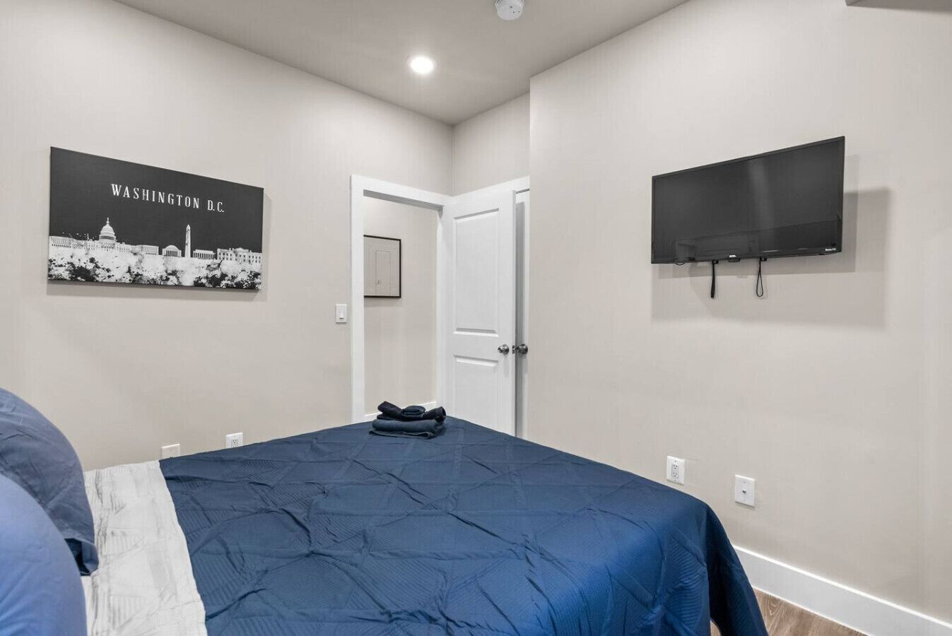 Une chambre dotée d’un grand lit, d’un téléviseur à écran plat fixé au mur et d’un tableau encadré représentant Washington D.C.