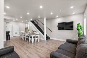 Un salon moderne avec un escalier, un coin repas et un téléviseur à écran plat fixé au mur.