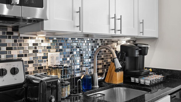 A modern kitchen with white cabinets, a black countertop, a stainless steel sink, a coffee maker, a toaster, and a kettle.