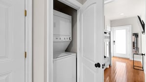 A laundry room with a washer and dryer, a door with a black handle, and a hallway leading to a room with a wooden floor.