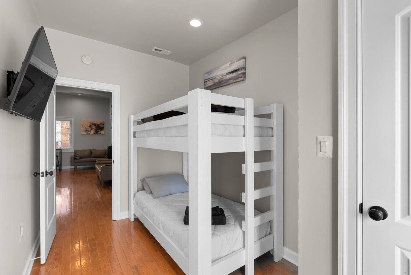 Une chambre avec un lit superposé, un téléviseur fixé au mur et une porte donnant sur une autre pièce.