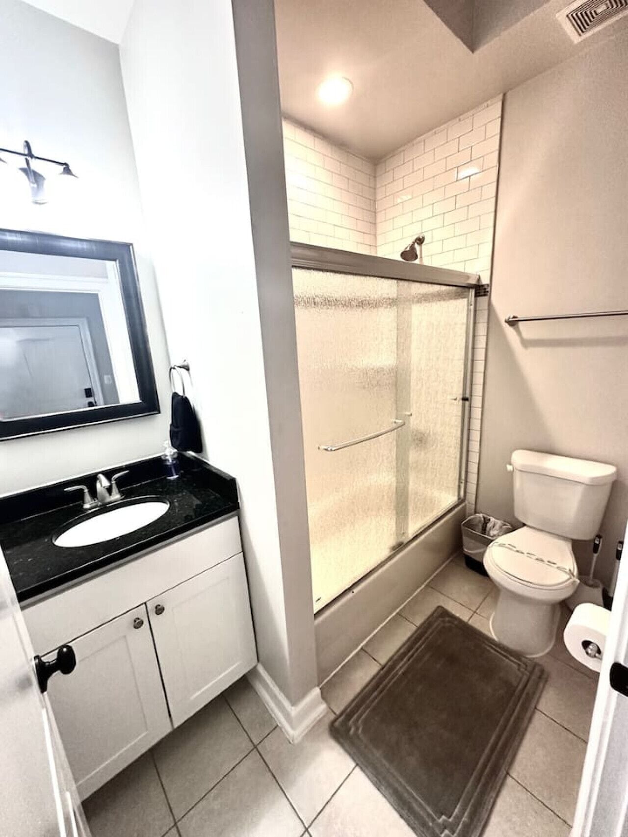 Un baño con lavamanos blanco, espejo, inodoro y ducha con puerta de cristal.