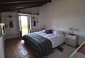 Un dormitorio con cama, mesitas de noche, una ventana y una puerta.