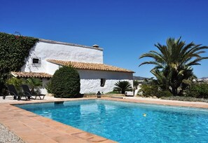 Una piscina con un edificio blanco al fondo, palmeras y un cielo azul despejado.