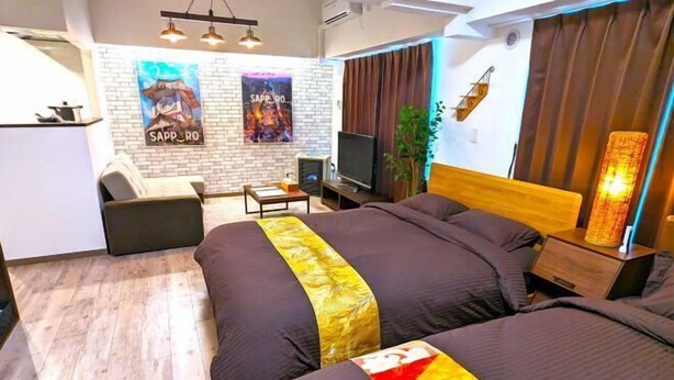 A modern hotel room with a large bed, a desk, a TV, and a brick wall with posters. - KIYAZA Station Sapporo 2 (Sapporo)