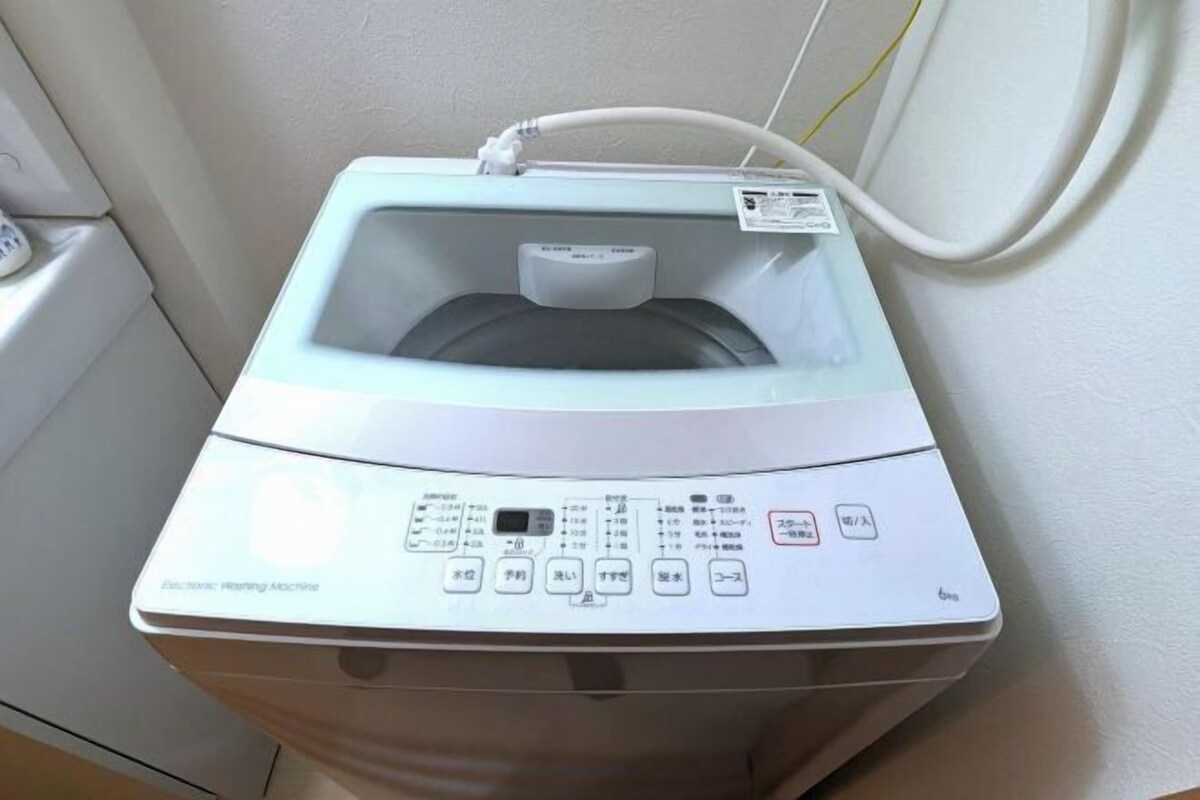 A front view of a washing machine with control panel and water inlet hose.