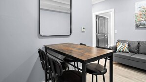 Un salon moderne avec une table à manger, des chaises, un canapé gris et un grand miroir au mur.
