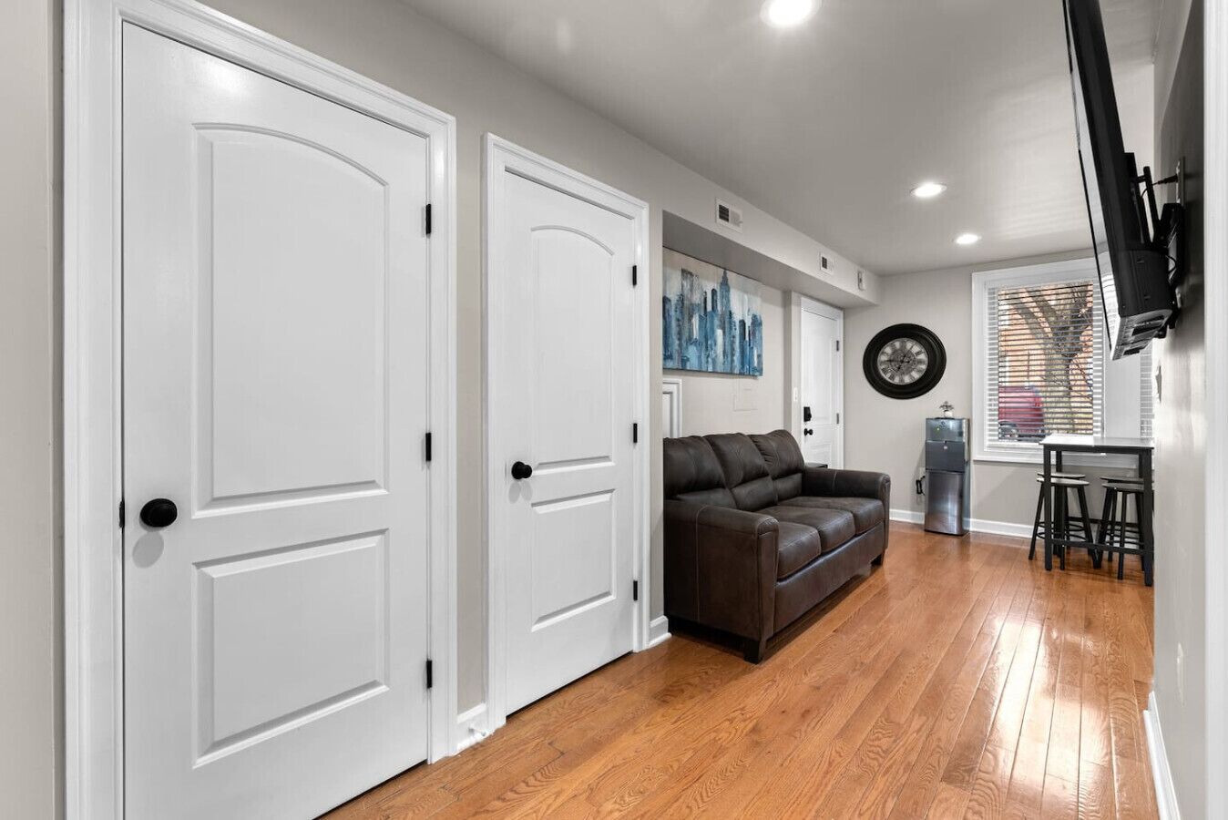 A spacious hallway with white doors, a brown leather sofa, and a dining area with a table and stools.