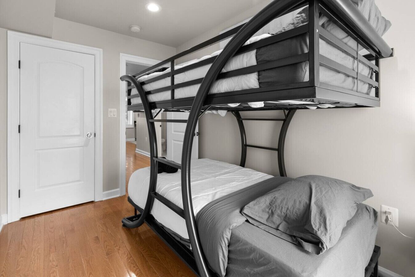 Una cama individual con estructura curvada, una puerta blanca y suelo de madera.