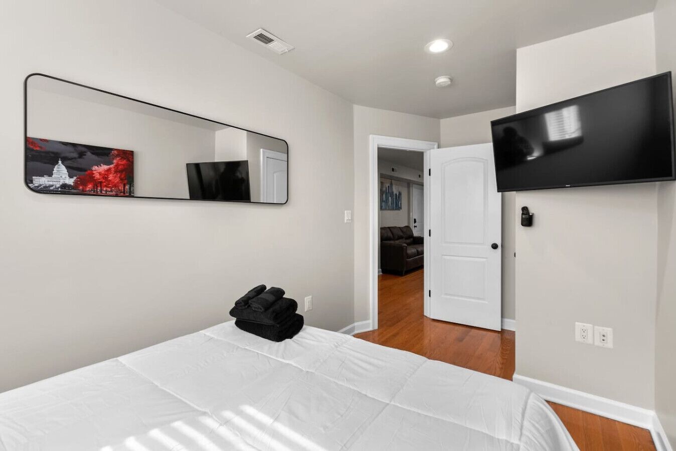 A bedroom with a bed, a mirror, a television, and a door leading to another room.