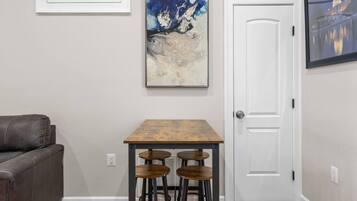A room with a gray wall, a white door, a brown table with stools, and a gray couch.