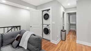 Un apartamento moderno con un sofá gris, una lavadora y un cubo de basura.