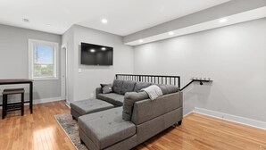 Una sala de estar moderna con un sofá seccional gris, una mesita y un televisor montado en la pared.
