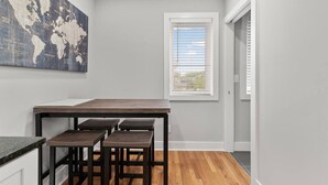 Una cocina con una mesa de madera y taburetes, un mapa del mundo en la pared y una ventana con persianas.