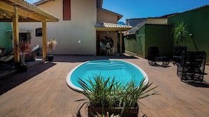 A swimming pool with a wooden deck, surrounded by potted plants and outdoor furniture. - Casa com Piscina e Churrasqueira no Pantanal (Angra dos Reis)