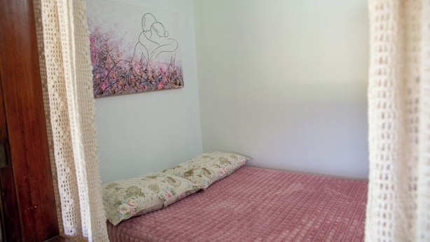 A bedroom with a bed, a floral-patterned pillow, and a wall painting of two people embracing. - Casa com Piscina e Churrasqueira no Pantanal (Angra dos Reis)