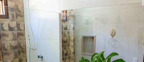 Un baño con cabina de ducha de vidrio, inodoro, lavabo con un espejo grande y una planta en el mostrador.