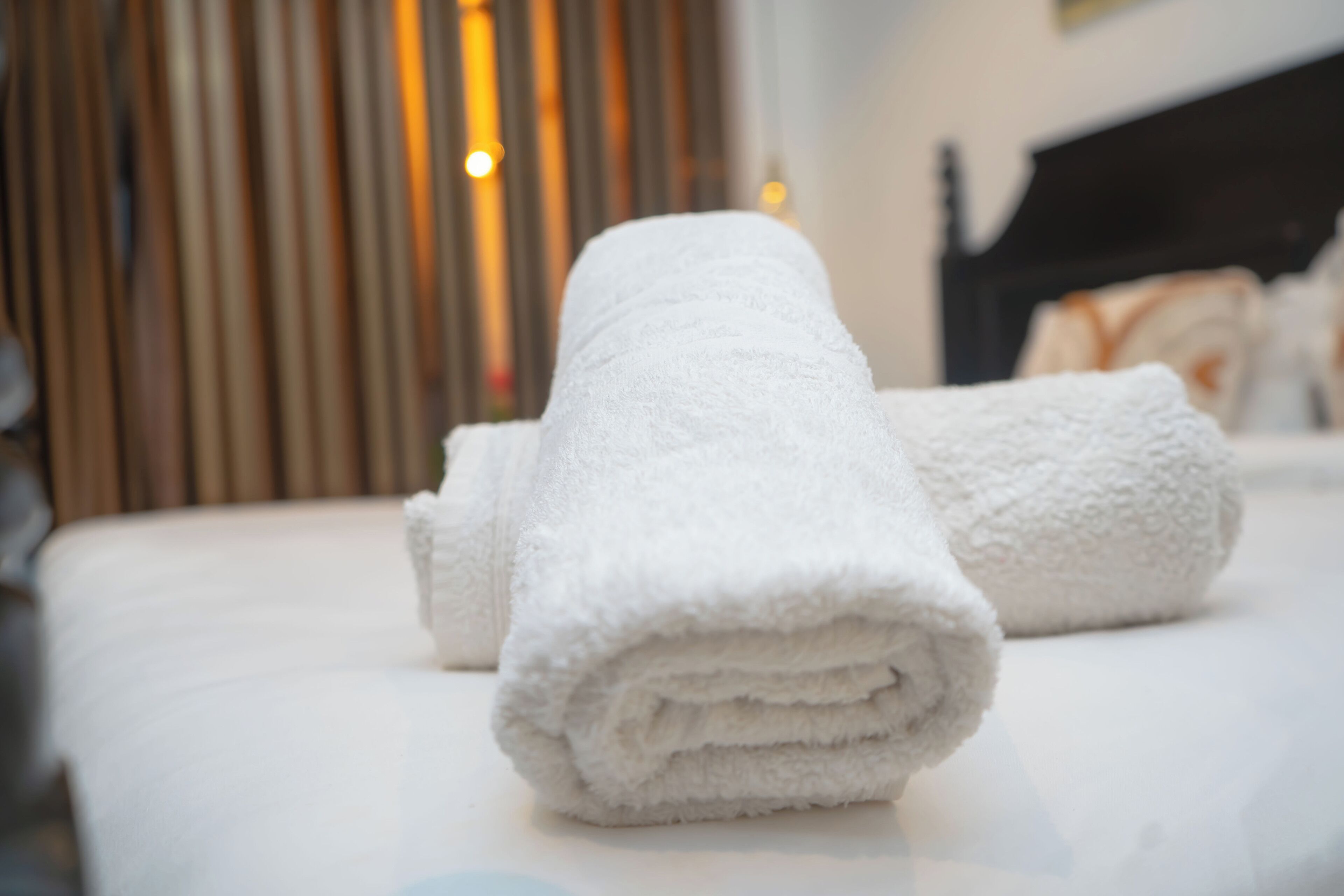 Een keurig opgevouwen witte handdoek op een bed in een hotelkamer.