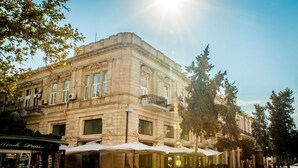 A historic building with large windows and a balcony, surrounded by trees and outdoor seating areas. - Bristol Baku Old City (Baku)