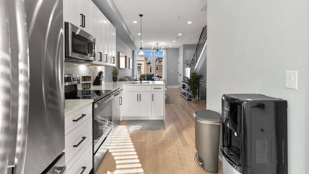 A modern kitchen with stainless steel appliances, a central island, and a view to the living area.