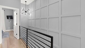 A hallway with a black railing, a ceiling light fixture, and a door leading to a room with a flat-screen TV.