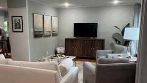 Ein Wohnzimmer mit einer Couch, einem Sessel, einem Fernseher und einem Schrank.