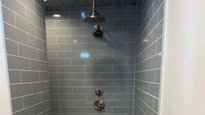 Eine Dusche mit grauen Fliesen, einem gemusterten Boden und einem weißen Handtuch auf der Ablagefläche.