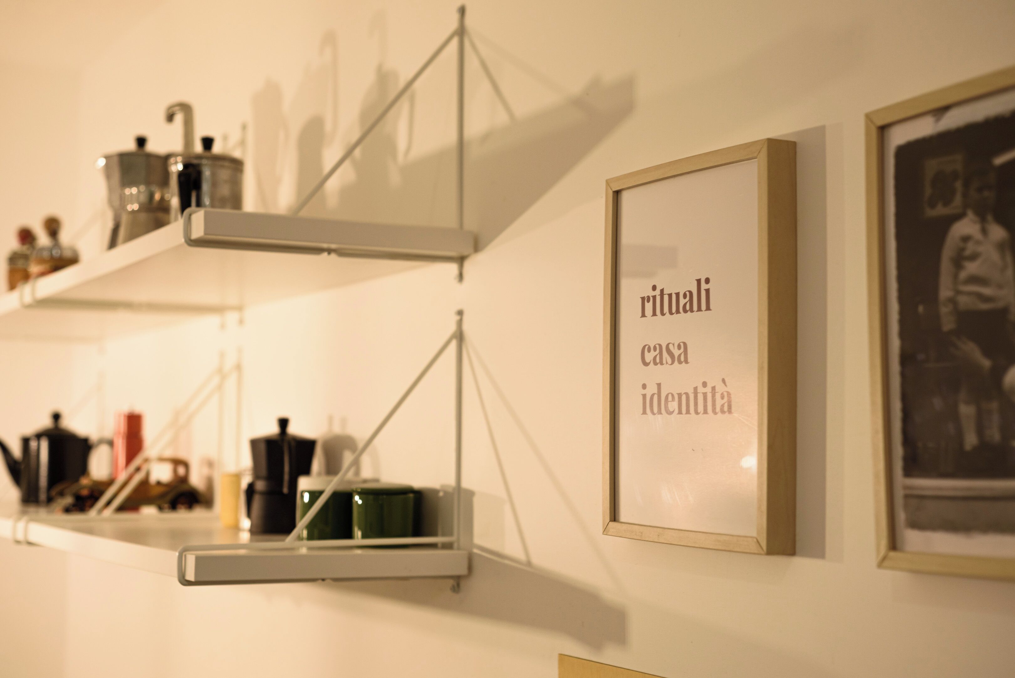 A wall with a framed text that reads "rituali casa identità" and a shelf with various items.