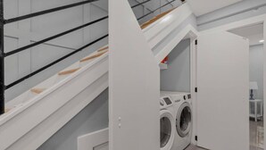 Une buanderie moderne avec un lave-linge et un sèche-linge intégrés, un escalier en bois et une petite table avec une lampe.