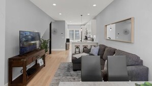 Un salon moderne avec un canapé gris, un meuble TV en bois et un coin repas comprenant une table et des chaises.