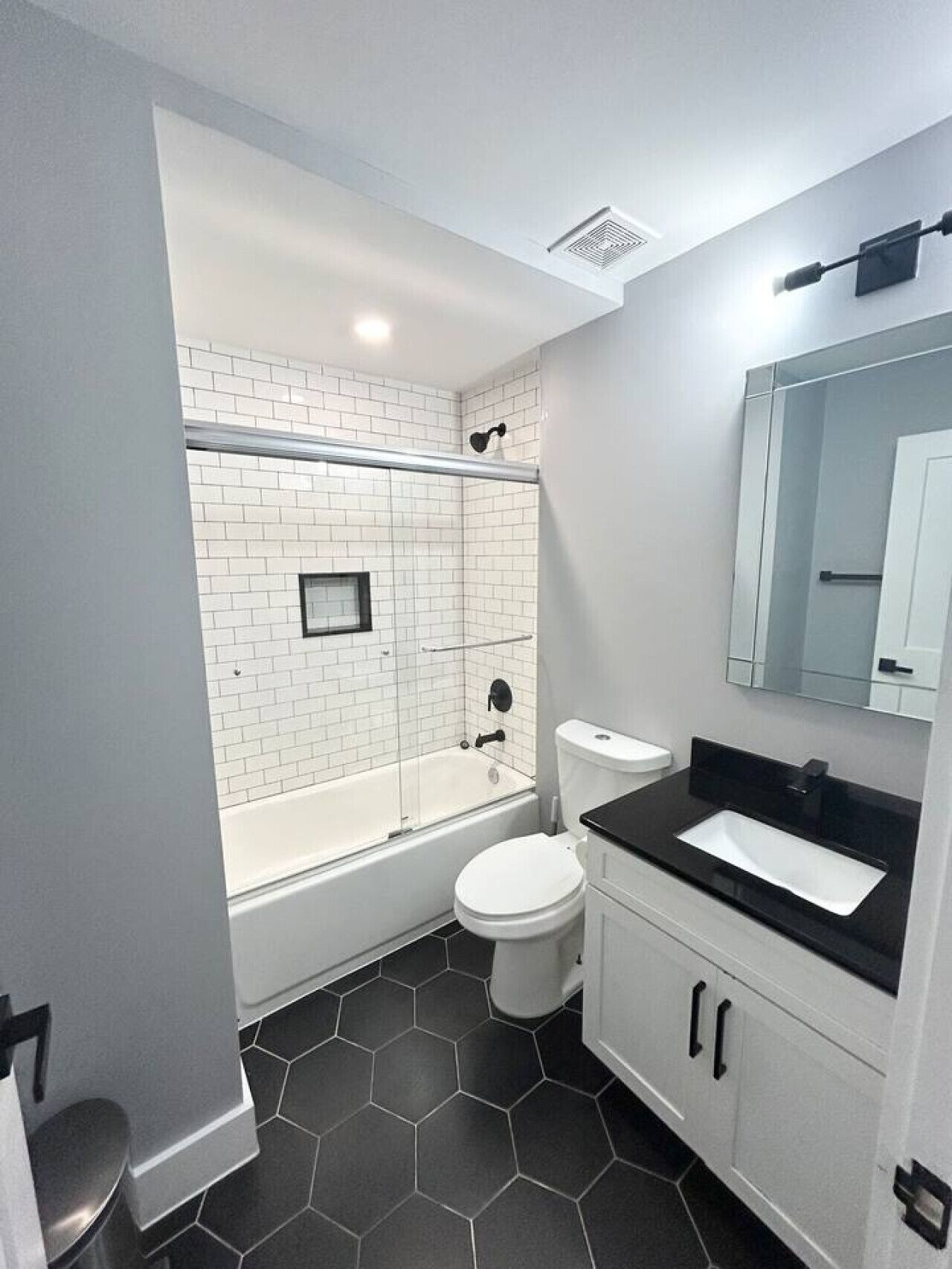 A modern bathroom with a white bathtub, a toilet, and a vanity with a black countertop.