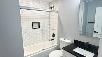 A modern bathroom with a white bathtub, a toilet, and a vanity with a black countertop.