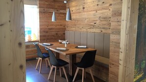 A wooden interior with a dining table, chairs, pendant lights, and a view of the outside. - Room 'Fedaia Joy Bnb Suite' with Mountain View, Balcony and Wi-Fi (Canazei)