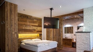A bedroom with a wooden headboard, a bed, a mounted TV, and a stone accent wall. - Room 'Fedaia Joy Bnb Suite' with Mountain View, Balcony and Wi-Fi (Canazei)