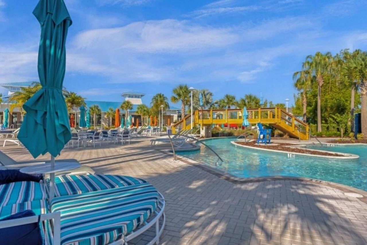 A pool area with lounge chairs and umbrellas, palm trees, and a yellow bridge.