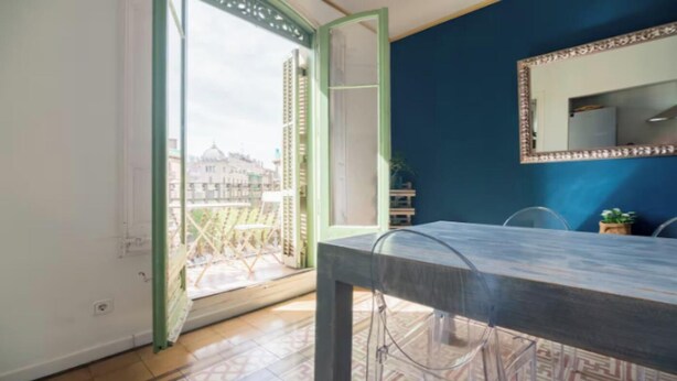 Ein Zimmer mit Balkon, einem Esstisch und einem Spiegel an der Wand.
