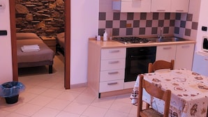 A compact kitchen with a stone wall, a gas stove, and a dining area with a table and chairs. - B&B linate (Peschiera Borromeo)