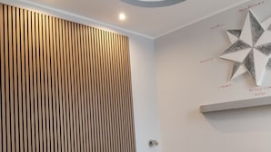 A modern bedroom with a wooden slatted headboard, a bed with a grey blanket, and a wall-mounted star decoration. - B&B linate (Peschiera Borromeo)