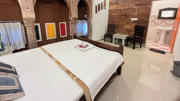 Une chambre d’hôtel avec un grand lit, une petite table, une chaise et une salle de bain avec un lavabo.