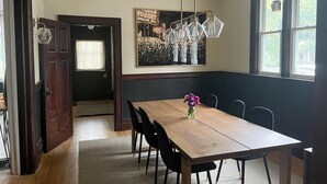 Een eetruimte met een houten tafel, zwarte stoelen, een hanglamp en een poster aan de muur.