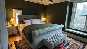 Een slaapkamer met een groot bed, een plafondventilator, een nachtkastje met een lamp en een raam met uitzicht.