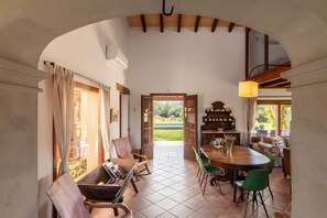 A dining area with a wooden table, chairs, and a view of a green landscape through an open door.
