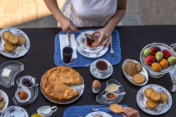 Una mesa dispuesta con diversos alimentos, como una tarta, magdalenas y frutas, con una persona sirviéndose.