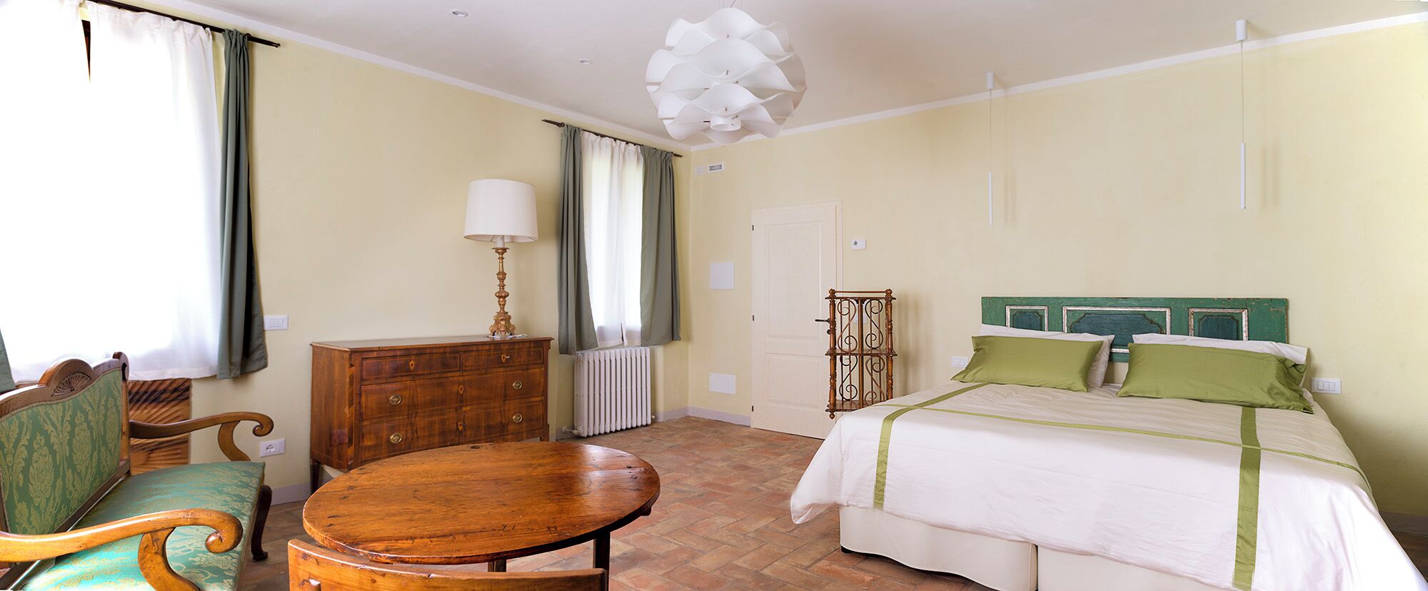 Un dormitorio con cama, una silla de madera, una mesa, un aparador y un radiador.